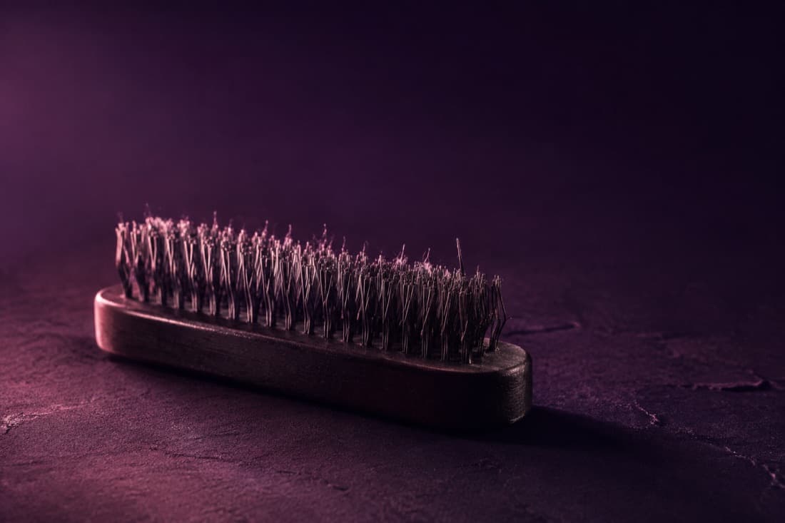 A steel-bristle suede brush lying on dark stone with lifted suede fibres in the wires